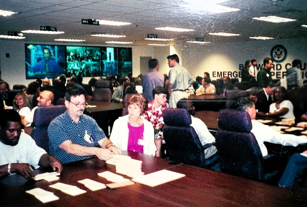 Volunteers and election workers in Broward County, Florida organized in groups around large tables preparing to review votes from the 2000 Presidential Election.