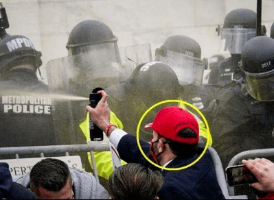 A January 6 rioter wearing a red Make America Great Again (MAGA) hat sprays Capitol Police with bear repellant.